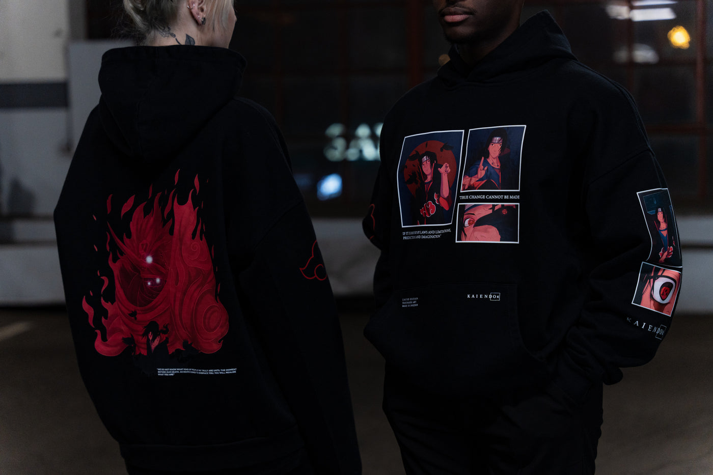 Two people wearing black hoodies with red anime graphics on back and sleeves, and stylized character prints on the front, from Kaiendo's anime fashion line